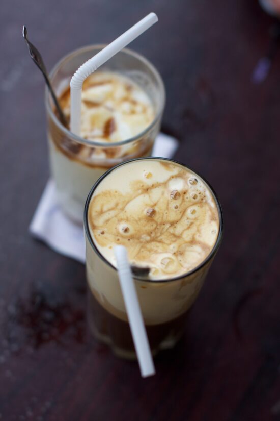 Close up of frothy iced vietnamese coffee in glass tumblers with white bendy straws and long tea spoons.