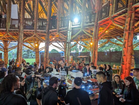 A huge group of coffee people gathered under a round wooden meeting hall structure with exposed beams and a walking terrace built on the second story.