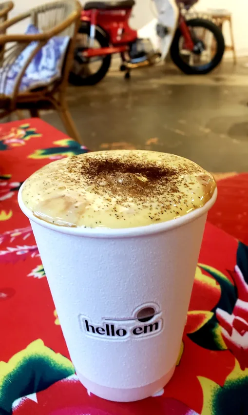 A frothy drink with spices on top in a paper hello em cup.
