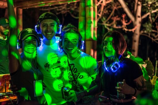Four people wear blue light-up over-ear headphones for the silent disco, all smiling and lit up with green polka dot lights at the Barista League Mystery Vacation.