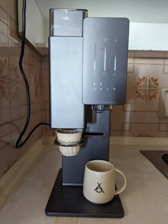 The xBloom is a tall, tower-shaped brewing device with a slim profile. On the top left is bean storage. Bottom right has a dock to hold the cup you;ll be brewing into. Top right is the control panel, which is streamlined and sleek, with backlights. A mug sits under the brew tower.