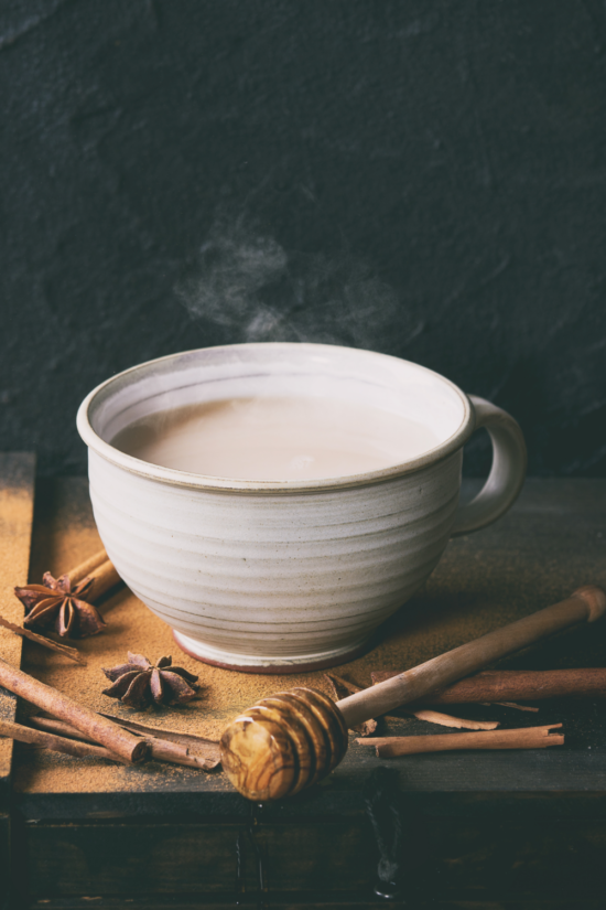 Steaming cup of chai with honey on a drizzle stick next to it.