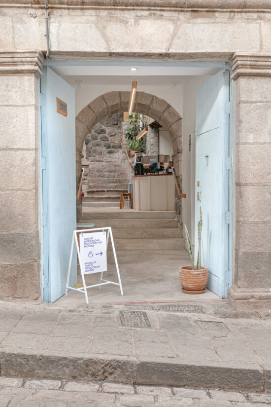 A sky blue double door leads up stairs to the cafe. At the front is a white sign hanging on an a frame that says "Specialty coffee produced by women" in both Spanish and English.