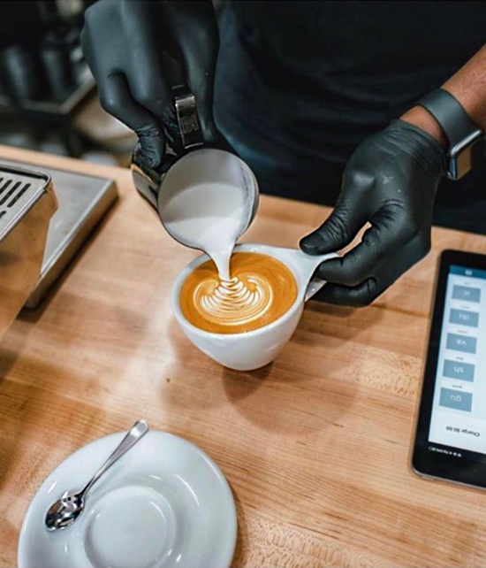 Two gloved hands pour a perfect rosetta into a white Not Neutral mug.