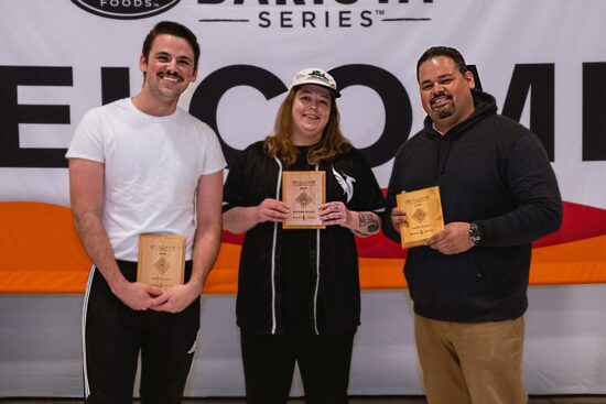 Three competitors in all neutral colors holding their wooden plaques.
