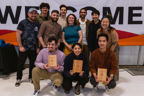 11 competitors, three with wooden plaques crouched in front, all smiling. 