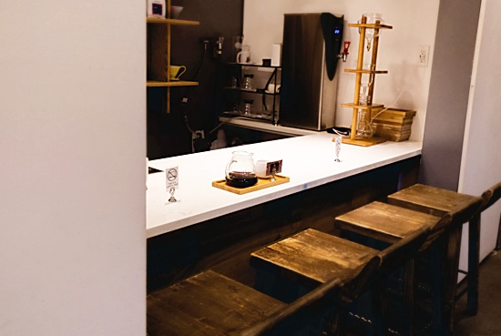 A small white counter with tall stools shows a Hario pour over set up for a customer, with Kyoto cold brew stands and other coffee implements behind the counter.