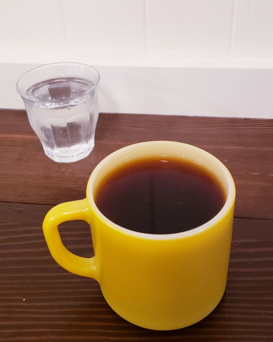Ethiopian coffee in a vintage yellow mug with a small glass of sparkling water on the side.