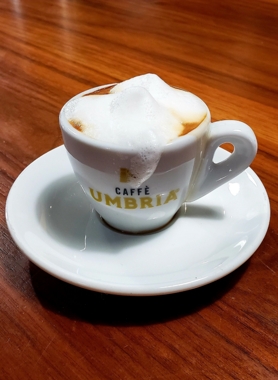 A macchiato in a tiny mug with the Caffe Umbria logo.