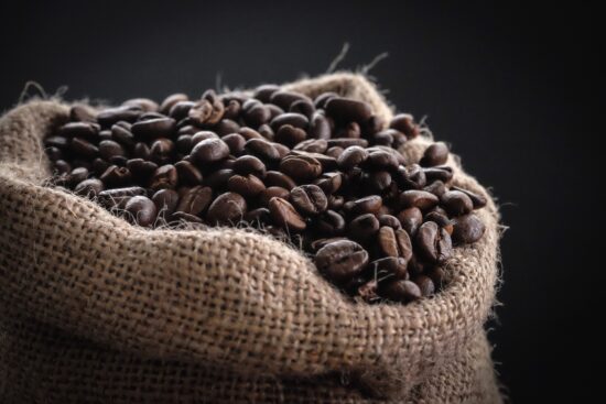 A close up of the top of a rough burlap sack filled to the brim with medium roasted coffee beans.