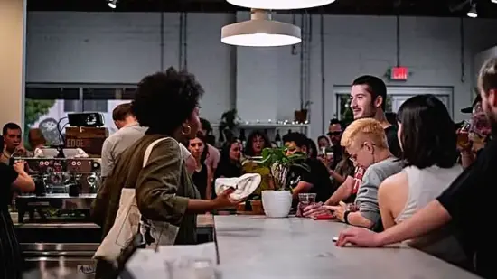 Baristas crowd around a white bar as people pull shots at an event.