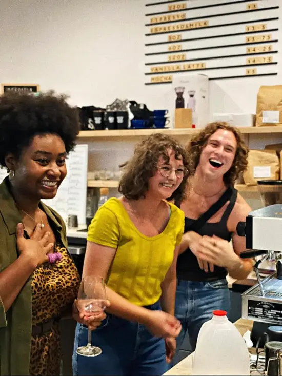 LaChrista and two baristas laugh together by an espresso machine. 