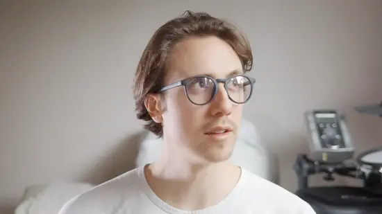 Dan wears glasses and a white shirt. He has shortis brown hair and looks off-camera.