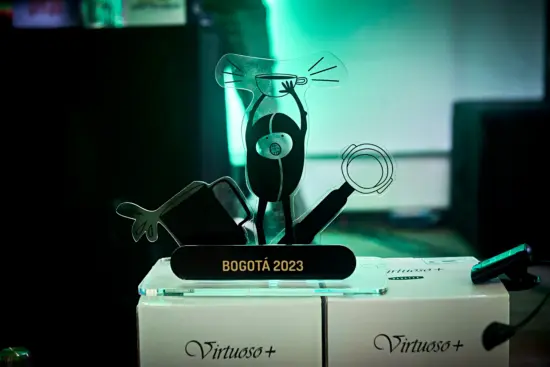 The trophy is a plastic etching of a small person in a bean shape holding up a big coffee cup. On the sides are a portafilter and steaming pitcher spilling milk. The plaque at the bottom says Bogota 2023.