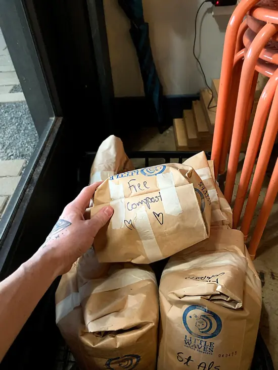A baristas stacks five-pound paper bags in a black cart, all taped at the top and labeled "Free Compost."