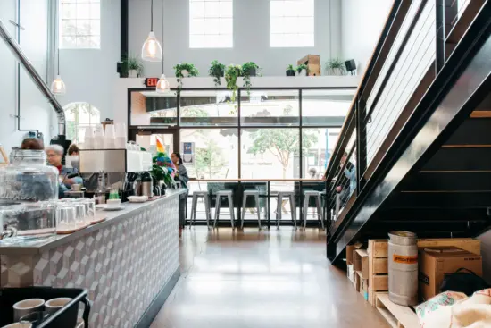 The inside of Guilder is a large open space with a wall of window, metal stools and chairs, a long metal bar, concrete floor, and staircase leading up to another floor on the right.