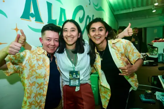 Carolina and Lorena wear matching flower shirts, and Ivette in the middle wears white and red pants. They pose for the camera with thumbs up and big smiles.