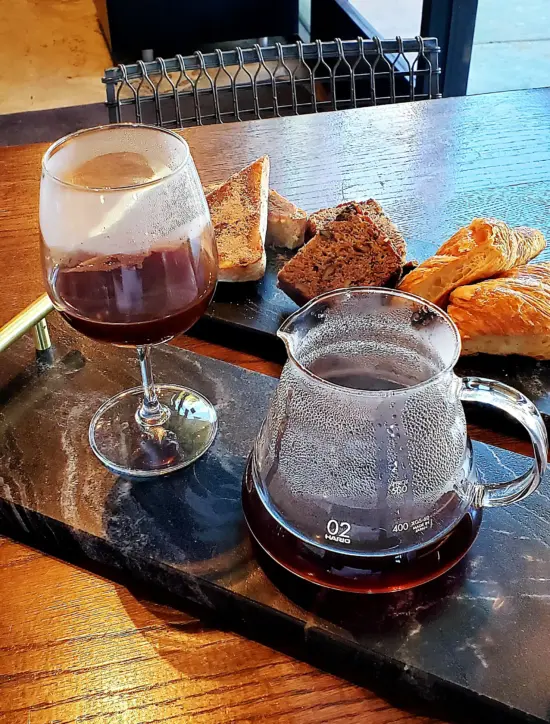 A marble tray holds a Hario 02 carafe, a stemmed wine glass, and another marble tray holds pastries.