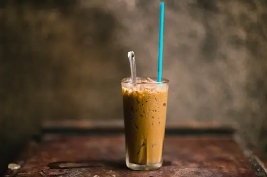 A Vietnamese iced coffee in a tall clear drinking glass with a long spoon and long blue straw.