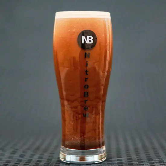 A flared pint glass similar to a Guinness glass. It has nitro coffee inside with bubbles cascading down the side, and The NitroBrew logo, an attached N and B.
