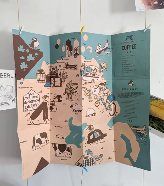 The inside of an older NI coffee map of the Causeway Coast. It features illustrations of people, plants, animals, and vehicles along with water features and points representing the featured coffee shops.