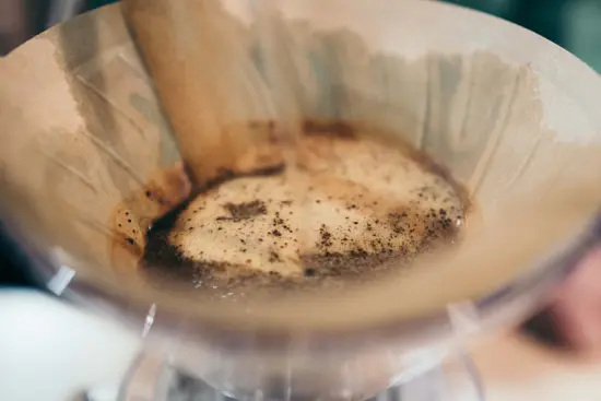 A close up view of coffee in a pour over cone, with the coffee blooming with just a bit of water.