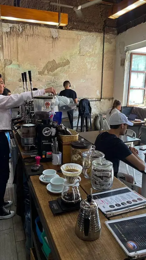 The busy inside of Fat Cat, with plaster walls, a long wooden bar with keg taps, and desserts and pour over coffees set up at the end of the bar. Large windows are open to the outside.