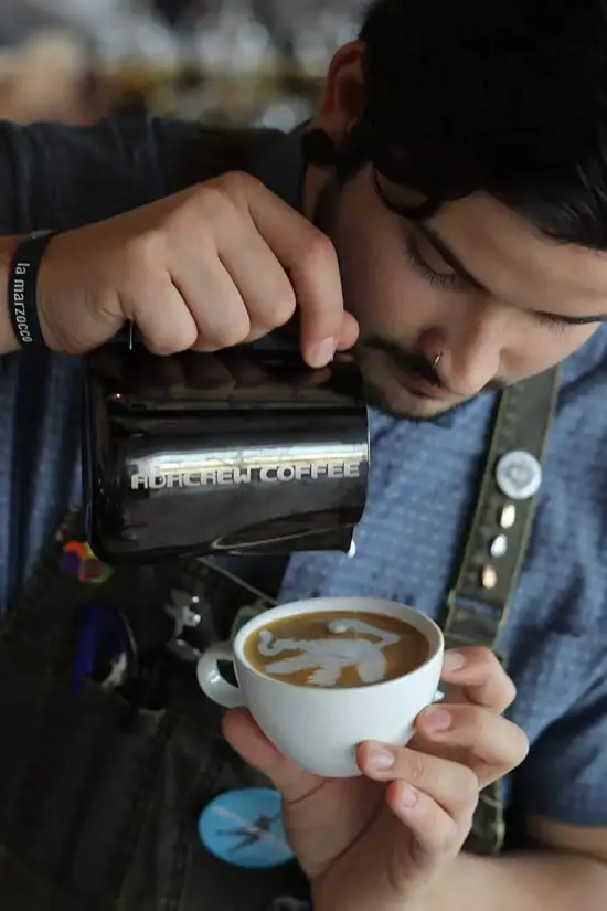 Juan pours a swan with outstretched wings into a latte.