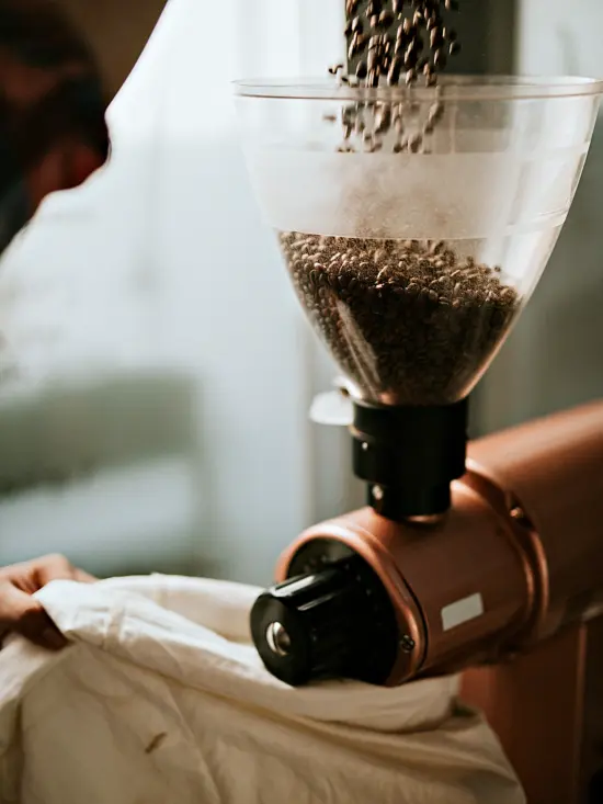 Beans are being poured into the top cone hopper of a large copper-colored grinder.