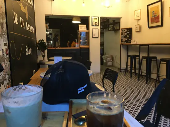 Inside Memorias are two long wooden bars for seating. Near the camera is a black hat with the words "coffee and people" printed on it. There is an iced milk drink and a black iced coffee.