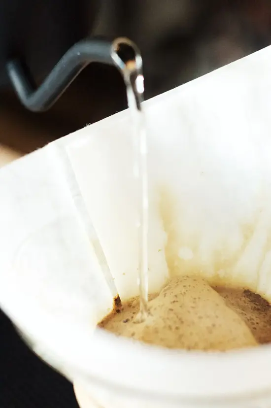 Close up of water being poured from a gooseneck kettle over coffee inside a pourover filter.