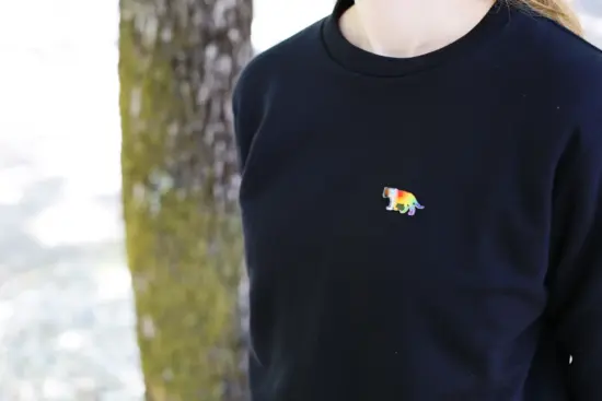 A person in a plain black shirt wears a pride rainbow pin shaped like a tiger.