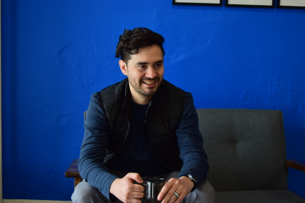 Paulo Melendez sits on a sofa with a cup of coffee in his hands.