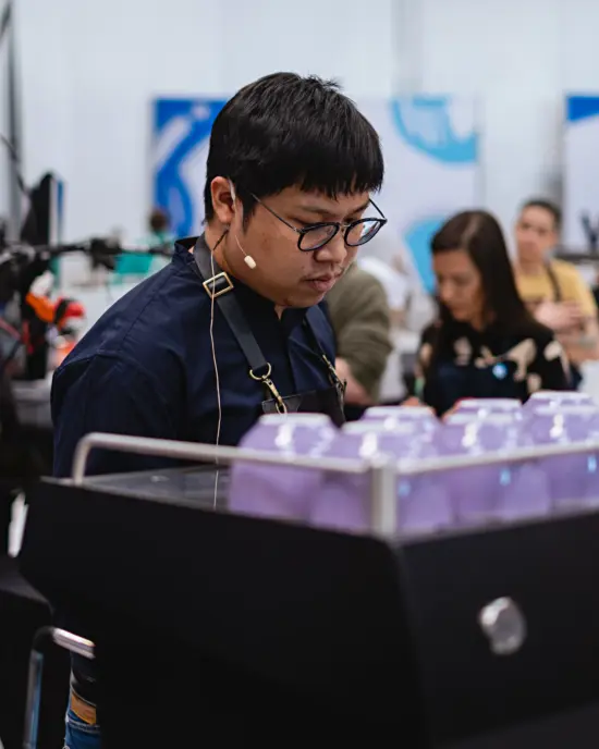 Flook in a nacy blue shirt and apron works on an espresso machine at the Denver Qualifiers.