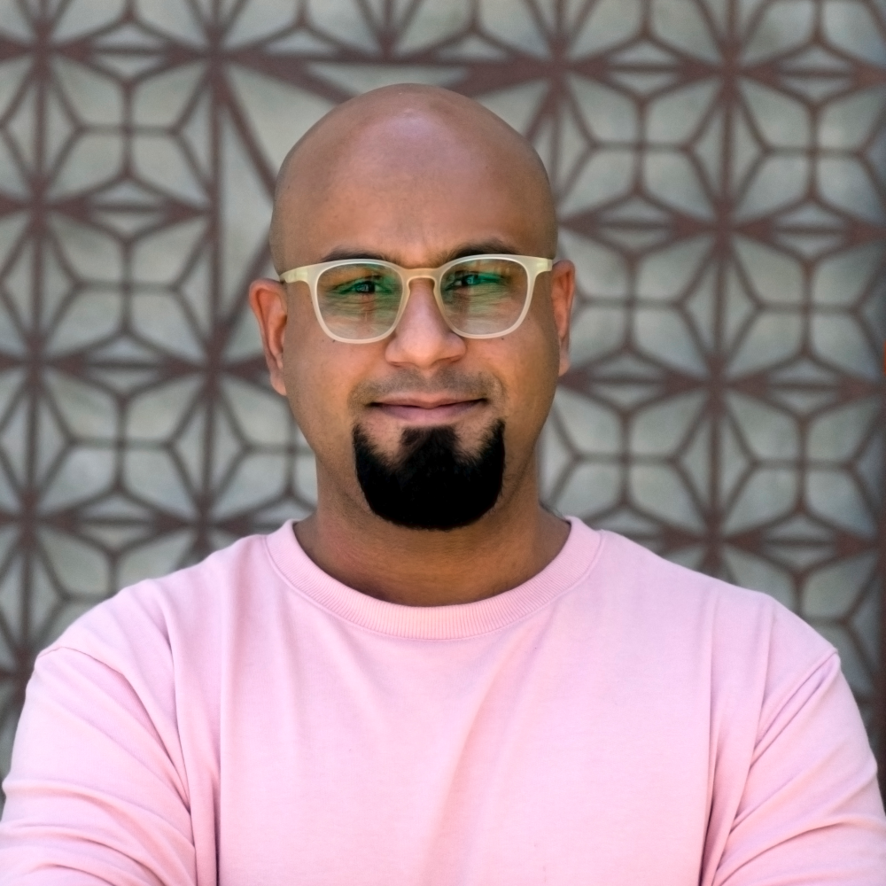 Jaseem Abbas wearing a pink shirt stands for a portrait.