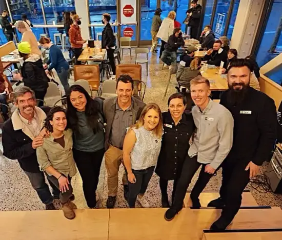 The panel, consisting of eight people, half men and hald women, pose together for a photo inside a cafe. 