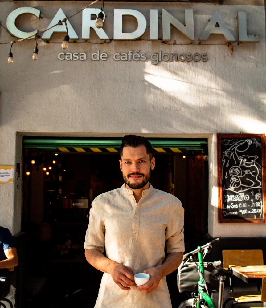 Edilberto Zapata poses in front of his café holding a ceramic coffee cup in his hands.
