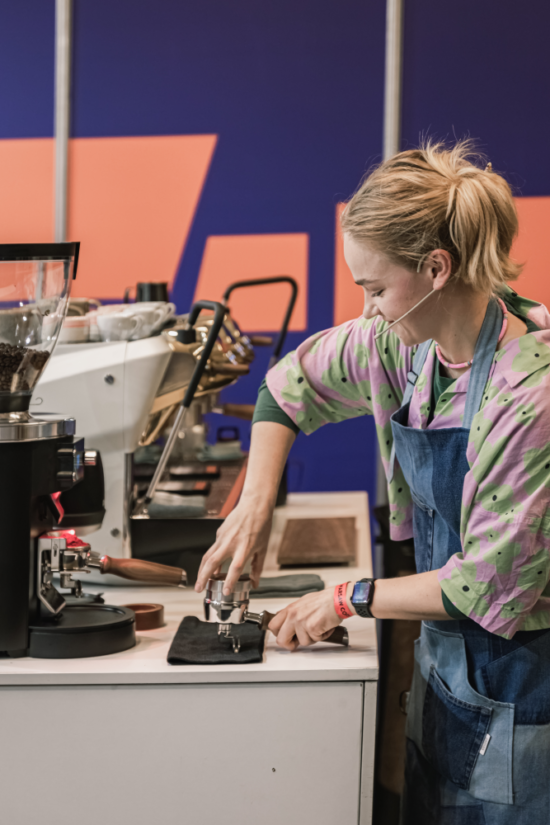 Dominika Kowalska tamps coffee in a portafilter on stage while competing in a barista competition to qualify for the World Barista Championship.