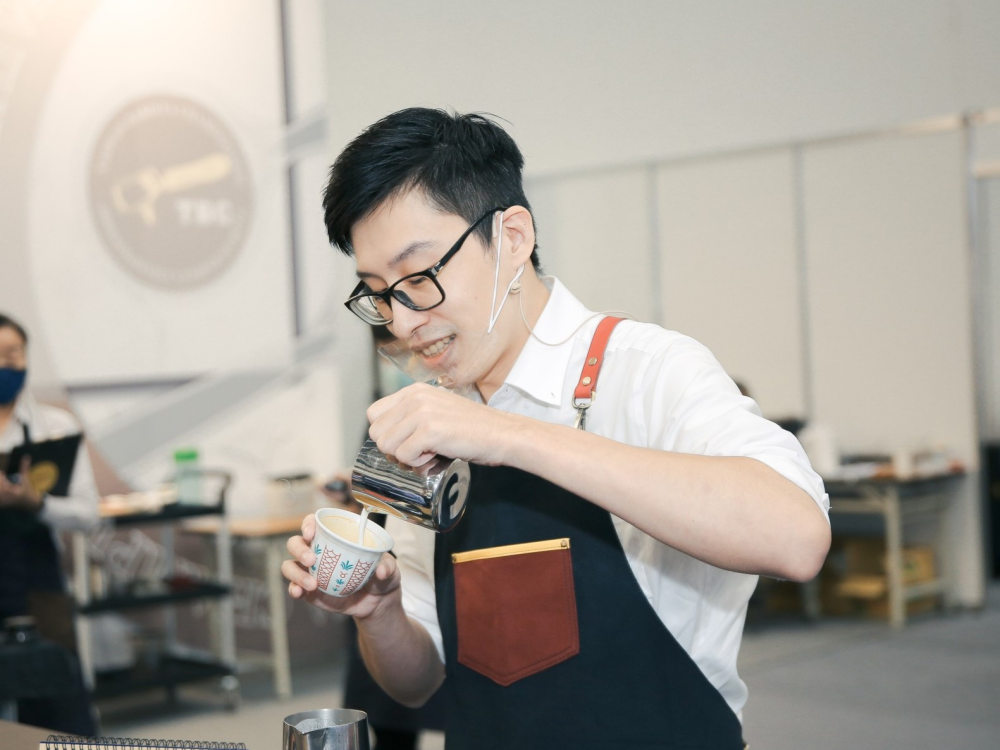 Hao-Yuan Chen pours steamed milk from a pitcher into a cup as he creates milk drinks during a barista competition.