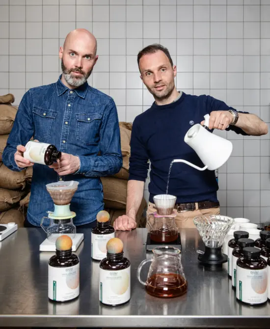 The two Depoorter brothers with V60s, ander® products, and bags of beans piled high behind them.