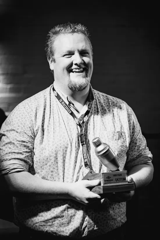 David in a black and white photo holding an award with a cocktail shaker on top.