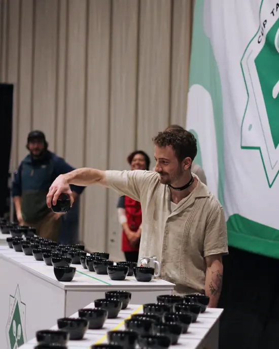 Jake holds up a black cupping vessel in his right hand. Rows of matching vessels are lined up on the table in front of him.