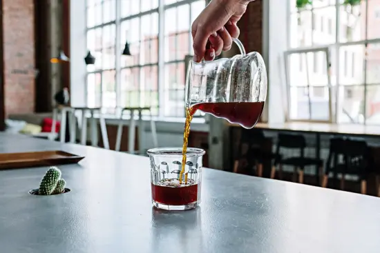 Pourover being being poured into a glass cup in a large room with big windows.