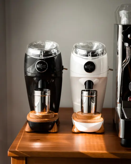 Two retro-inspired grinders, one black and one white, with chrome and wooden feet.