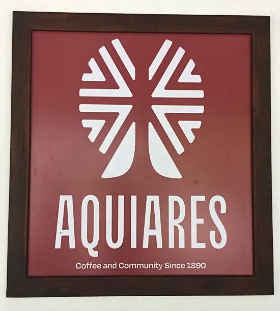 A red sign in a wooden frame with the farm's logo and the words: Aquiares, Coffee and Community Since 1890.