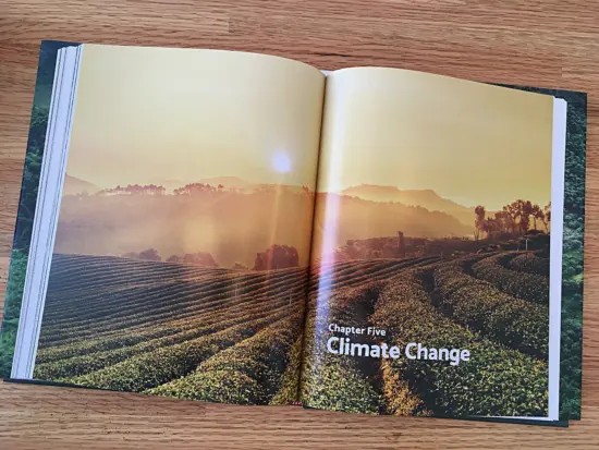Book opened to chapter five, Climate Change. These two pages form one photo of a coffee plantation from above, with rows and rows of growing trees, and the sun rising behind the hills, washing the landscape in warm yellow light.