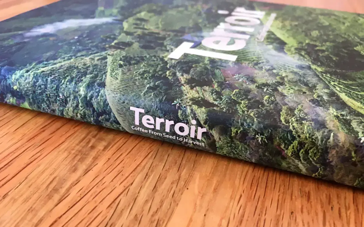 Vista lateral del lomo del libro titulado 'Terroir: Coffee from Seed to Harvest'. La portada muestra una vista reducida de una finca cafetalera desde arriba.