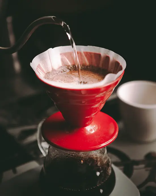 A red V60 pourover device being filled with water over a clear glass server.