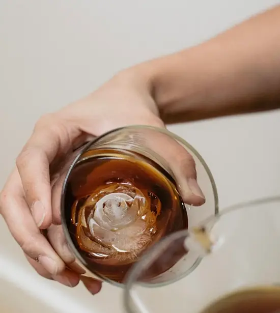 A hand hold a glass sideways to show off an ice cube shaped like the opening bud of a rose.