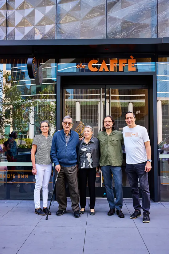 The family, two older women, one older man, and two ounger men pose outside the new cafe's doors. 